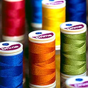 May include: An assortment of colourful spools of thread, each with a white label that reads "Prime". The spools are arranged in a row, with the colours red, blue, yellow, green, and orange.