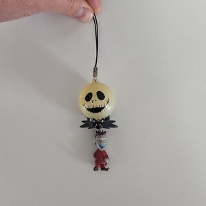 May include: A black and yellow Jack Skellington charm with a red and black Jack Skellington figure hanging from it.