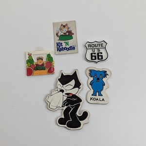 May include: Five vintage iron-on patches. A black and white cat with a white handkerchief, a blue koala, a red and green cartoon cat with the text "Kit 'N Kaboodle", a red and white cartoon bear with a red hat, and a white and black sign with the text "ROUTE U.S. 66".