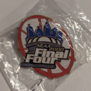 May include: A pin from the NCAA 2000 Final Four in Indianapolis. The pin is oval-shaped with a basketball design in red and white. The pin features a blue skyline and the text "NCAA 2000 Final Four Indianapolis".