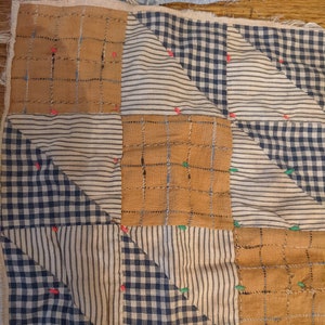 May include: A quilt block made of brown and blue fabric with a checkered pattern. The block is made up of nine smaller squares, each with a different pattern. The block is pinned together with red and green pins.