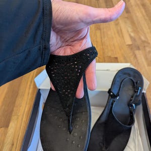 May include: A pair of black leather sandals with a cut-out design. The sandals have a buckle closure and a comfortable footbed.