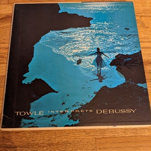 May include: Album cover featuring a woman in a dress standing in the ocean, with a blue and black color scheme. The text "TOWLE INTERPRETS DEBUSSY" is printed in gold.