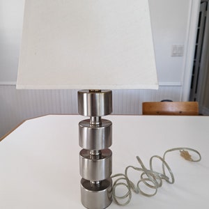 May include: A silver table lamp with a white lampshade. The lamp base is made of stacked cylinders.
