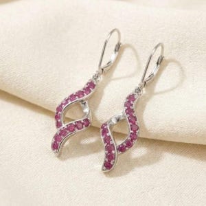 May include: A pair of silver-toned dangle earrings featuring a twisted, open-loop design. Each earring is encrusted with small, round, vibrant pinkish-red gemstones set along the front surface, finished with a secure lever-back closure.