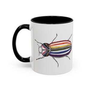 May include: White ceramic mug with a black handle and interior. The mug features a colorful illustration of a beetle with a rainbow-striped body and a Union Jack design on its head. The design is a whimsical and artistic representation.