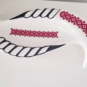 May include: White ceramic serving dish with a black and red geometric design. The dish is shaped like a crescent moon and has a raised rim.