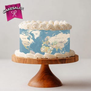 May include: A round cake decorated with a world map design, topped with white frosting. The cake sits on a wooden cake stand. The logo "Cakesalot" is in the upper left corner.