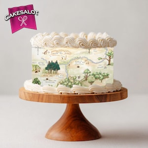 May include: A rectangular cake with a map design, topped with white frosting, sits on a wooden cake stand. The map features illustrations of trees, houses, and text. The cake has a pink banner with the text "Cakesalot" and a logo.