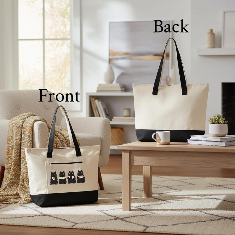 May include: Two canvas tote bags, one in front and one in the back, with black bottoms and handles. The front bag has a black zipper pocket and a graphic of four black cats. The bags are on a light wood table.
