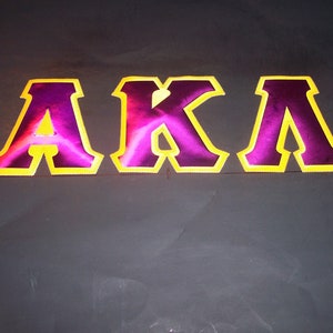 May include: A close-up of a sign with the letters "AKA" in large, bold, purple letters with a yellow outline.