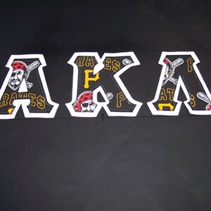 May include: Black, white, and yellow embroidered patches spelling out "AKA". Each letter features a pirate with a baseball bat and the word "PIRATES". The patches have a white border.