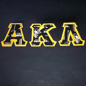 May include: Yellow felt letters spelling "AKA" with a Pittsburgh Penguins hockey team logo on each letter.