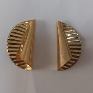 May include: A pair of gold-toned earrings. Each earring features a half-circle shape with a ridged, fan-like design on one side and a smooth, triangular shape on the other. The earrings have a polished finish.