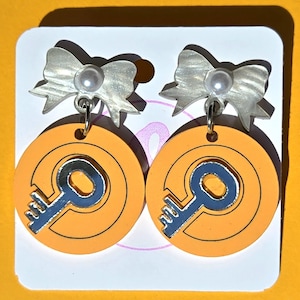 May include: A pair of orange and silver key-shaped earrings with a white pearl and bow charm.