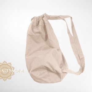 May include: A beige drawstring bag with a long strap. The bag is made of a soft, natural fabric.