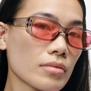 May include: A person wearing a pair of clear, rectangular sunglasses with pink lenses. The sunglasses have a slightly rounded shape and are worn on the person's face.