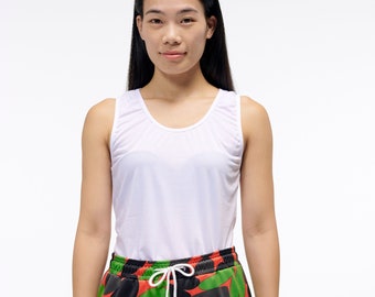 May include: A woman wearing a white tank top and green, red, and black patterned pants.
