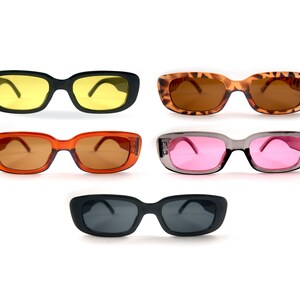 May include: Five pairs of rectangular sunglasses with different colored lenses. The sunglasses have black, brown, gray, and orange frames.