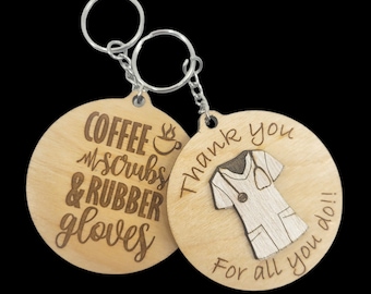 May include: Two wooden keychains with a silver key ring. One keychain has the text "Coffee, Scrubs & Rubber Gloves" with a coffee cup icon. The other keychain has the text "Thank you for all you do!" with a stylized image of a nurse's uniform.