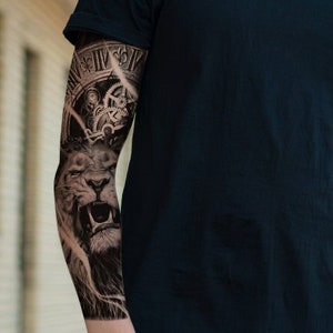 May include: A man wearing a black t-shirt with a large lion and clock tattoo on his left arm. He is wearing black sunglasses and a black watch.