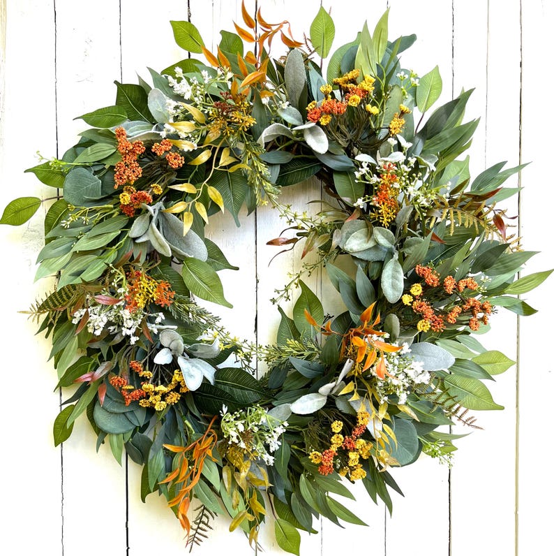 May include: A green, orange, and white artificial floral wreath with a variety of leaves and flowers. The wreath is made of silk and is perfect for adding a touch of nature to your home decor.