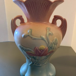 May include: A vintage ceramic vase with a pink, blue, and green glaze. The vase features a floral design with a large pink flower and green leaves. The vase has two handles and a flared opening.