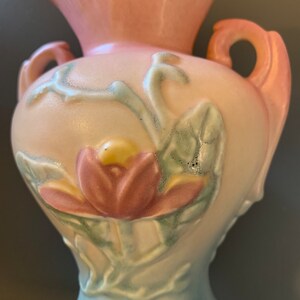 May include: A vintage ceramic vase with a pink, white, and blue glaze. The vase features a raised floral design with a pink flower and green leaves.