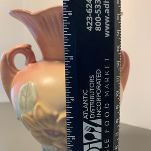 May include: A pink and white ceramic vase with a floral design. The vase is approximately 6 inches tall and has a wide mouth. The vase is sitting on a table next to a ruler.