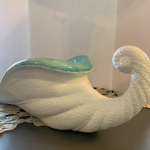 May include: White ceramic cornucopia with a light blue glaze on the inside. The cornucopia has a textured surface and a curled handle.