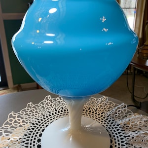 May include: A light blue glass vase with a bulbous body and a white, twisted stem. The vase sits on a white circular base. The vase is approximately 12 inches tall.