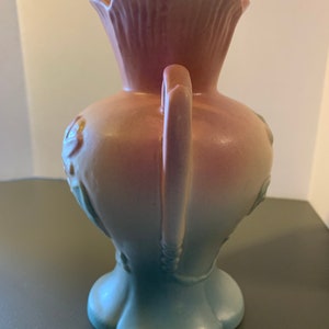 May include: A pink and blue ceramic vase with a handle and floral design. The vase has a gradient color scheme, transitioning from pink at the top to blue at the bottom.