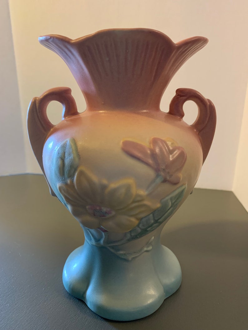 May include: A vintage, hand-painted, pink, yellow, and blue ceramic vase with two handles and a floral design. The vase has a scalloped rim and a flared base.