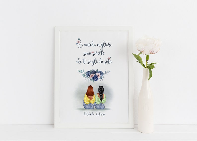 May include: A framed art print featuring an illustration of two figures with brown and black hair, seated together. The print includes the text "Le amiche migliori sono sorelle che ti scegli da sola" and floral accents. A white vase with a flower is to the right.
