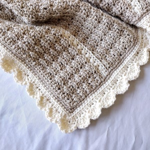 May include: A handmade crochet blanket in shades of brown and cream. The blanket features a textured stitch pattern and a scalloped edge. The soft, neutral colors make it a versatile home decor item.