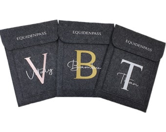 May include: Three gray felt laptop sleeves with the word "EQUIDENPASS" printed on the top. Each sleeve has a different letter embroidered on the front: a pink "V" with the word "Vlady" underneath, a gold "B" with the word "Bambu" underneath, and a white "T" with the word "Titan" underneath.