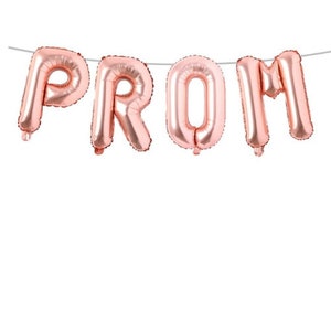 May include: Rose gold foil balloons spelling out the word "PROM" are strung on a thin, silver string. The balloons are inflated and have a metallic sheen, perfect for a prom celebration. The background is plain white.