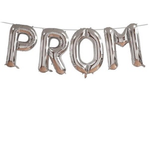 May include: Silver foil balloons spelling out the word "PROM" are strung on a thin white string. The balloons are inflated and have a reflective surface, with a metallic sheen. The letters are large and easily readable against a white background.