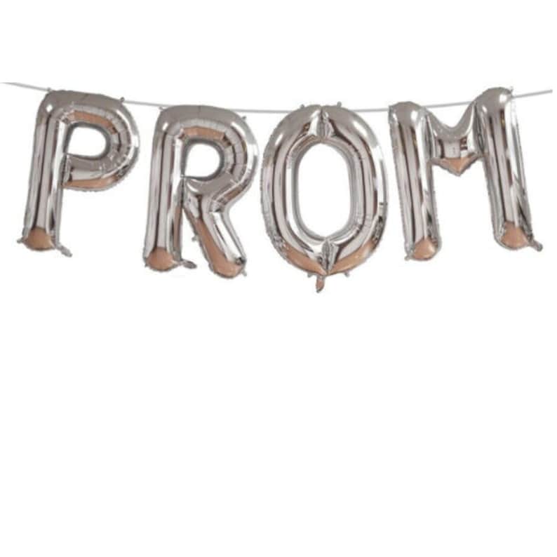 May include: Silver foil balloons spelling out the word "PROM" are strung on a thin white string. The balloons are inflated and have a reflective surface, with a metallic sheen. The letters are large and easily readable against a white background.