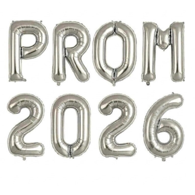 May include: Silver foil balloons spelling out "PROM 2026". The balloons are inflated and arranged in two rows. The top row spells "PROM", and the bottom row spells "2026". The balloons are metallic and reflective.