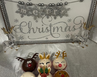 May include: A festive display featuring Christmas-themed treats. The treats include reindeer, unicorn, polar bear, and gingerbread man designs. A decorative sign with the words "Merry Christmas" is in the background, along with silver reindeer figurines.