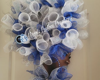 May include: A decorative wreath featuring a profile of a face adorned with voluminous white, silver, and royal blue mesh loops. The design includes a large mesh bow at the base and the text Virgo's Custom Creations overlaid on the center.