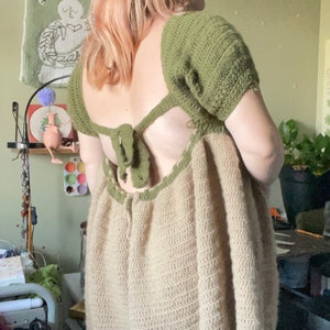 May include: A crochet dress with a green top and a beige bottom. The dress has a low back with a green tie. The dress is loose fitting and has a flowy skirt.