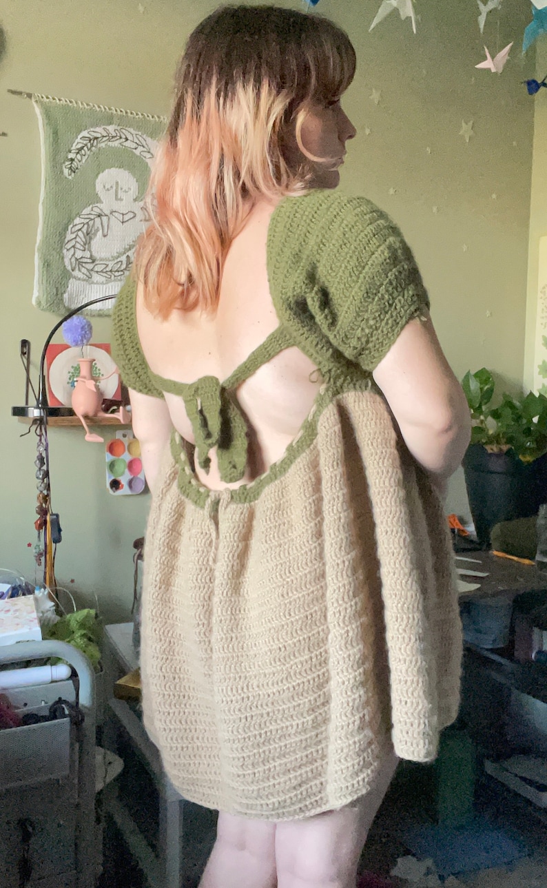 May include: A crochet dress with a green top and a beige bottom. The dress has a low back with a green tie. The dress is loose fitting and has a flowy skirt.