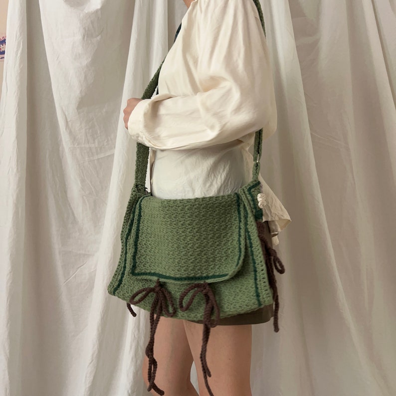 Peut inclure: Un sac &agrave; bandouli&egrave;re en crochet vert avec des sangles en cuir marron et une fermeture &agrave; rabat. Le sac a un design tiss&eacute; textur&eacute; et est port&eacute; sur l'&eacute;paule.
