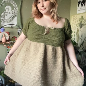 May include: A green and beige crochet dress with a tie at the neckline. The dress has a fitted bodice and a flowy skirt.