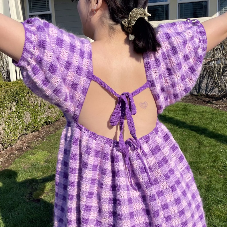 May include: A purple and white gingham crochet dress with a low back and a tie closure. The dress has a loose fit and is perfect for a summer day.
