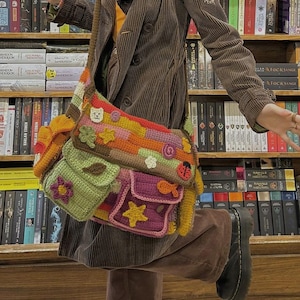 Pu&ograve; includere: Una giacca di velluto a coste marrone con una borsa all'uncinetto colorata con diverse tasche e decorazioni. La borsa ha un design a forma di fiore, stella, coccinella e pesce.