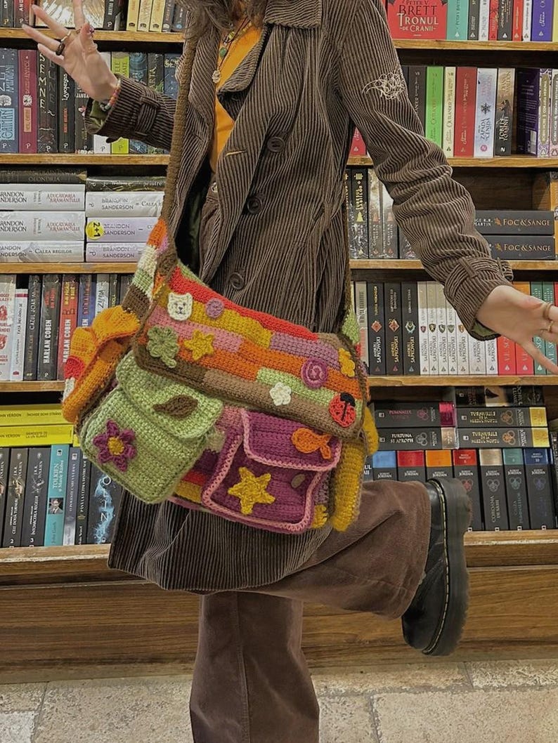 Pu&ograve; includere: Una giacca di velluto a coste marrone con una borsa all'uncinetto colorata con diverse tasche e decorazioni. La borsa ha un design a forma di fiore, stella, coccinella e pesce.