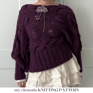 May include: A deep purple long-sleeve sweater featuring a cable knit pattern with leaf motifs, a wide ribbed hem, and a boat neckline. A delicate silver-toned floral pendant necklace rests on the chest. Text reads: my clematis KNITTING PATTERN.